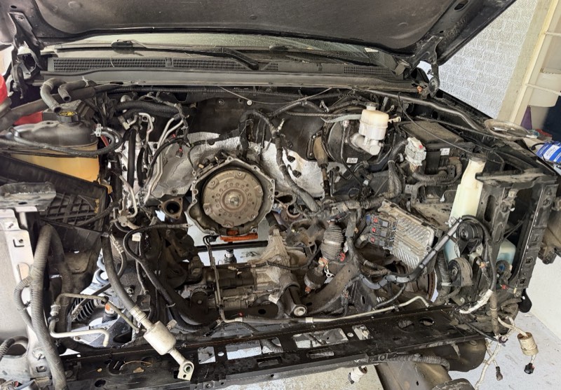An empty engine bay with the engine removed, showing the transmission bell housing and the wiring around it.
