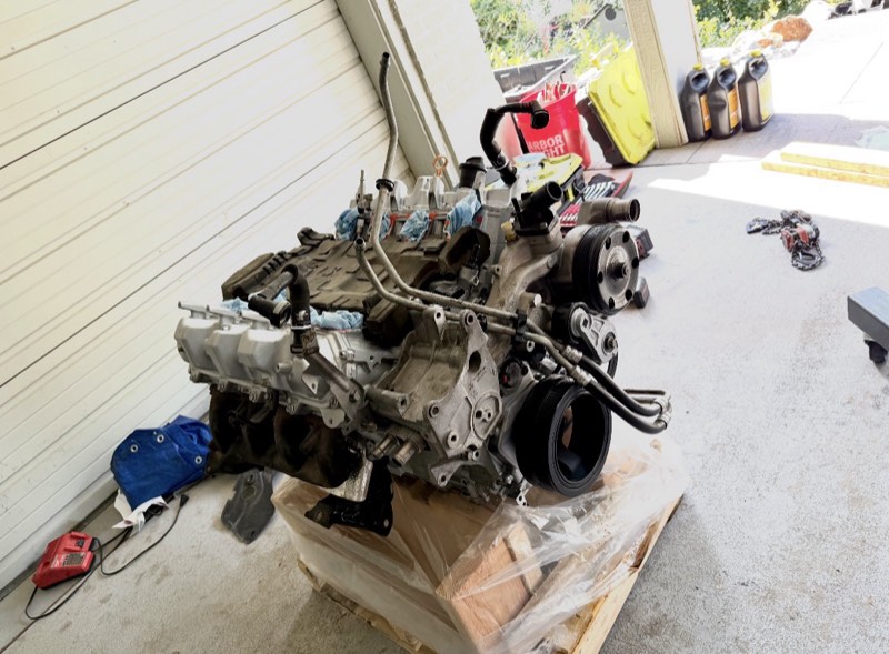 An engine sitting on a pallet next to a garage door in a carport.